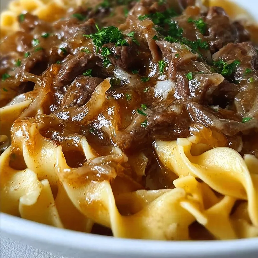 Bowl of French onion beef and noodles garnished with herbs.