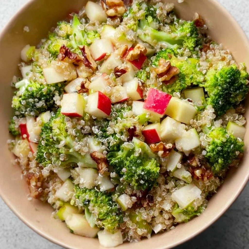 Delicious broccoli apple quinoa salad in a bowl, topped with nuts and dressing.